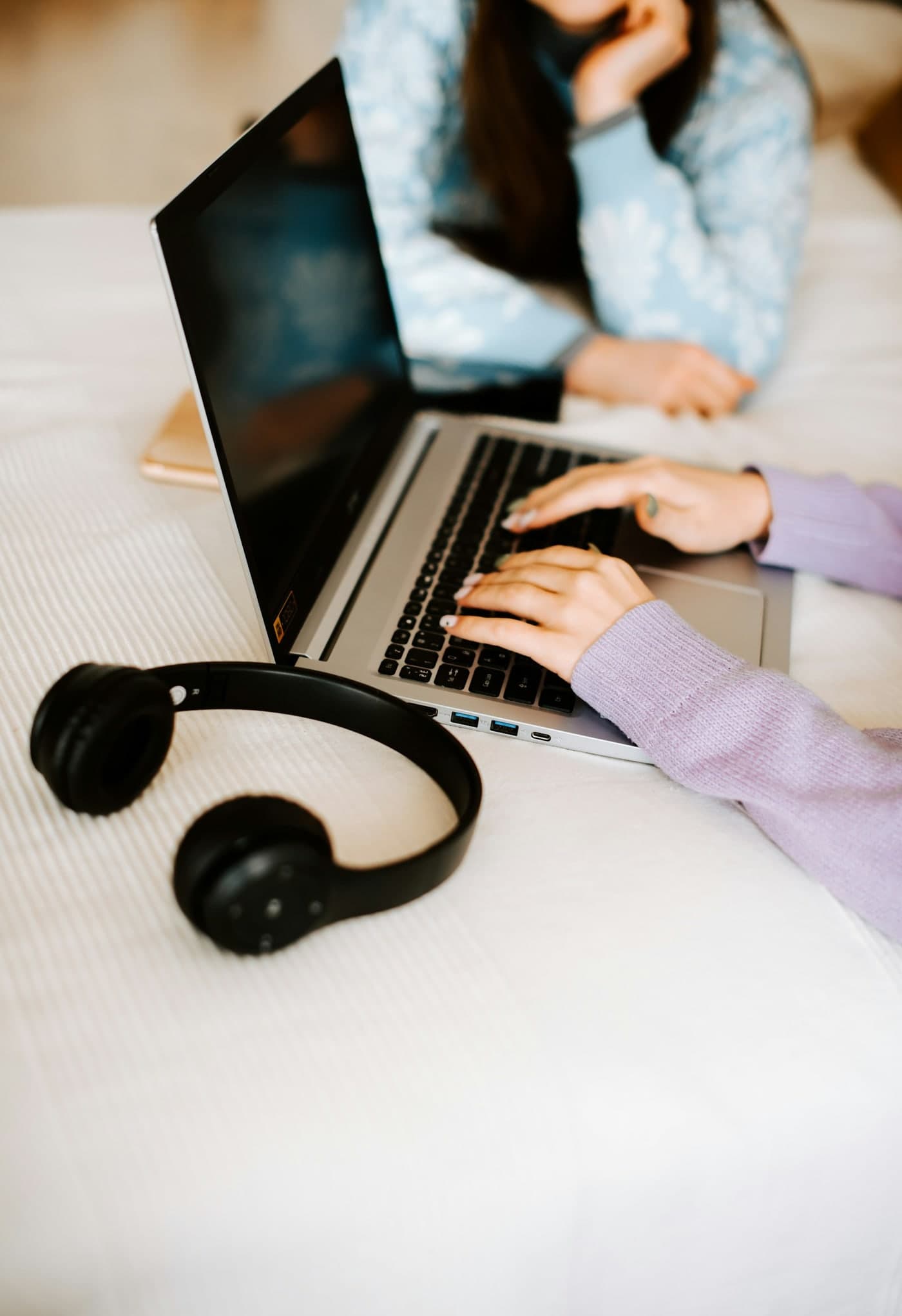 Hands typing on a laptop beside a pair of headphones