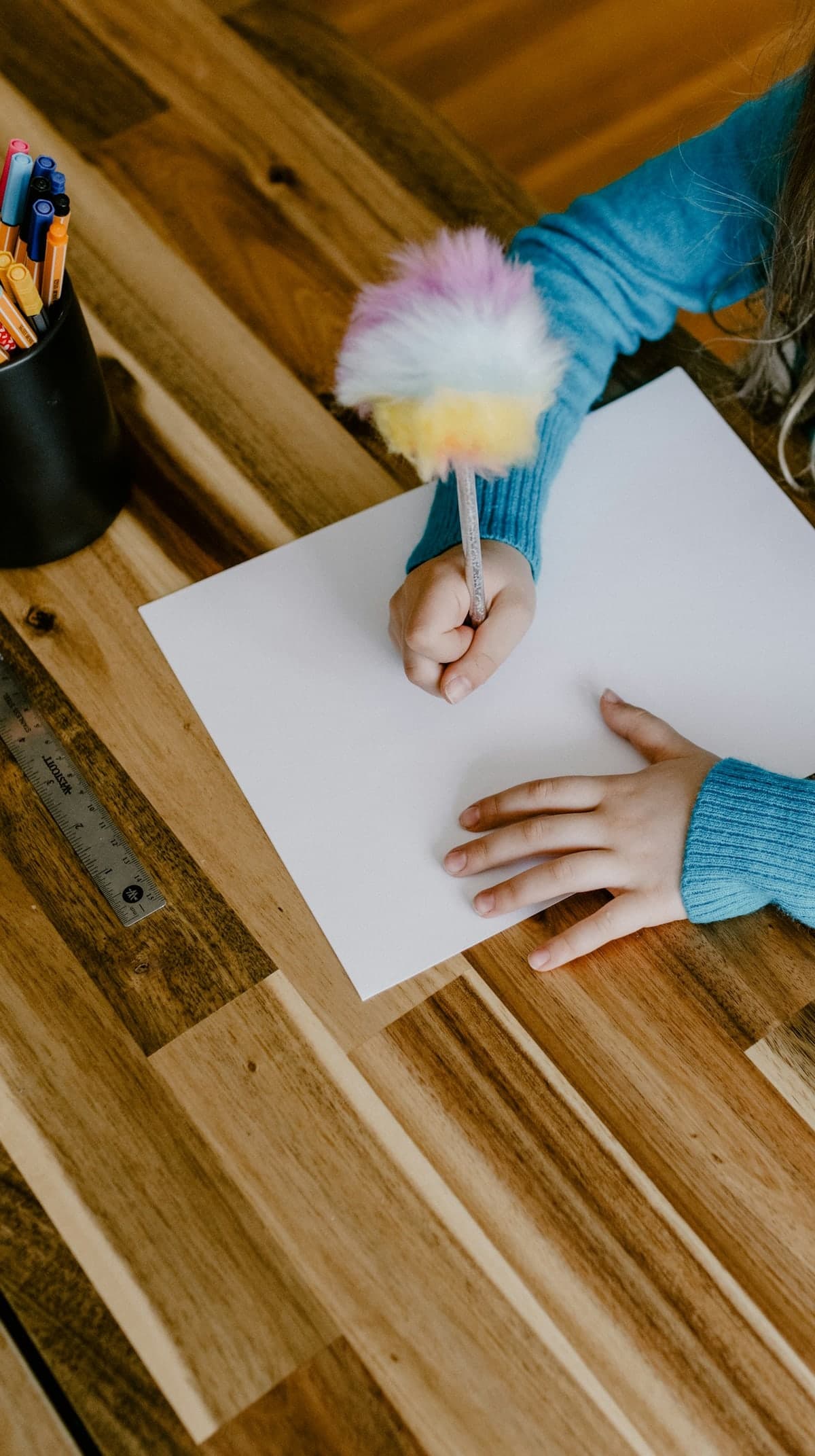 A child's hands writing on a sheet of paper at a wooden desk
